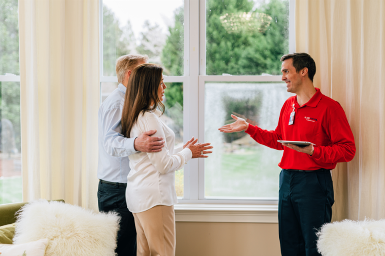 a male Glass Doctor service professional, man, and woman standing near a foggy window inside of a home
